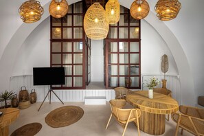 A dining area with a round table, wicker chairs, and a large window with curtains. - Villa located in Lindos (Rhodes)