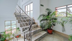 A staircase with metal railings leading to an upper floor, surrounded by potted plants and large windows.