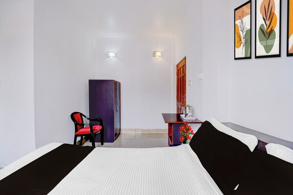 A hotel room with a bed, a desk with a chair, a wardrobe, and a door.