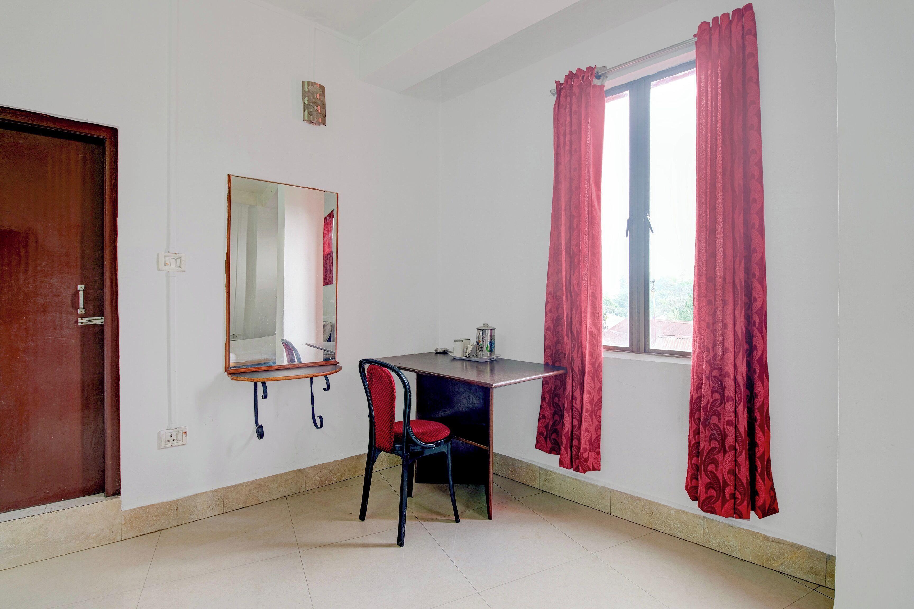 Een kamer met een bureau, stoel, spiegel en een raam met gordijnen.