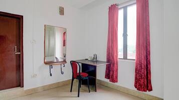 Een kamer met een bureau, stoel, spiegel en een raam met gordijnen.