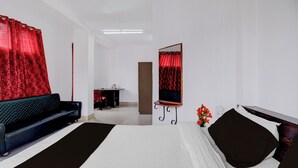 A modern bedroom with a large bed, a black sofa, a small desk, and a mirror on the wall.