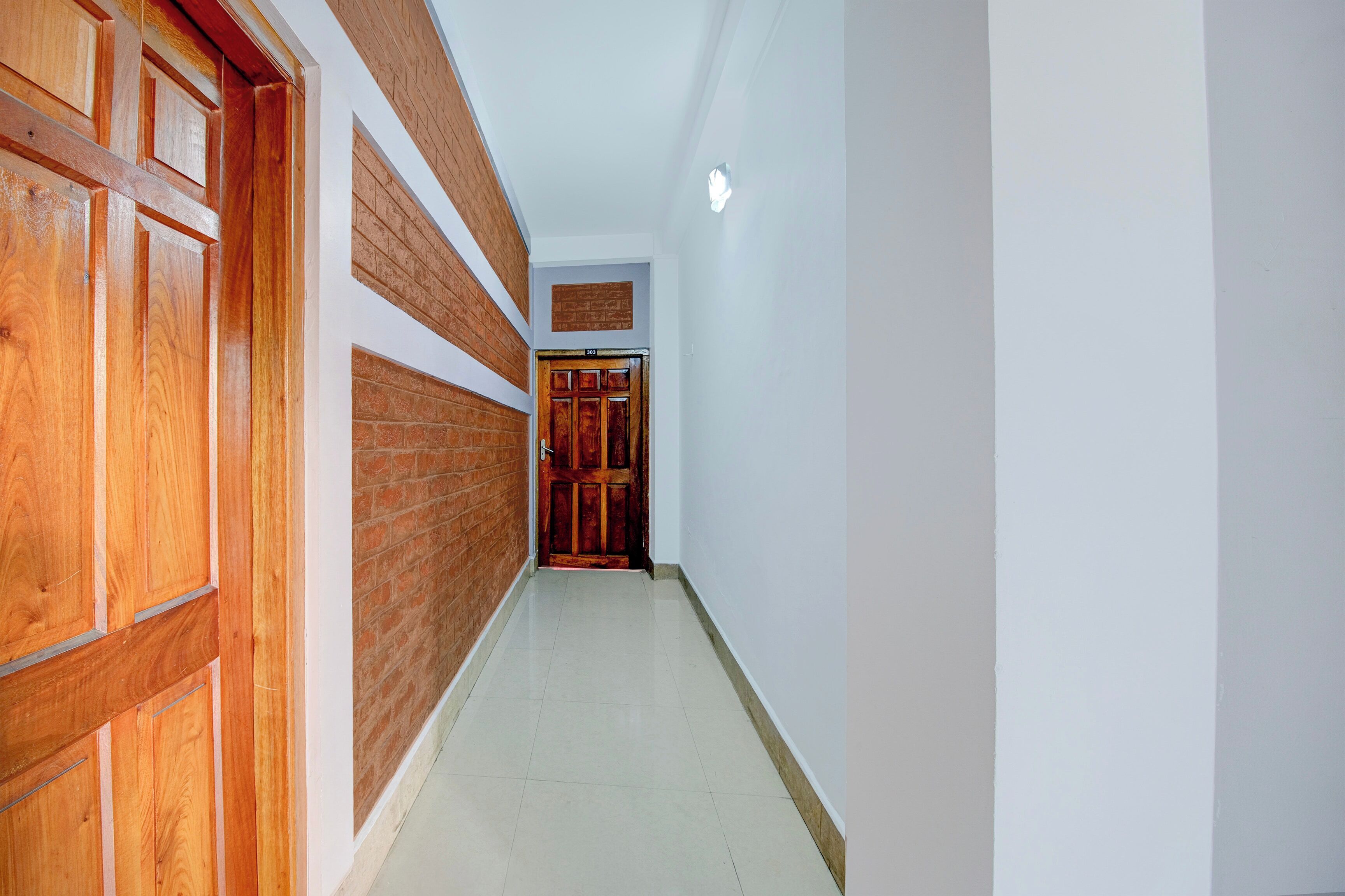 A corridor with wooden doors on one side and a brick wall on the other, leading to a door marked with the number 303.