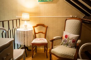 Una habitación con una silla de madera, una mesa con mantel de encaje, una lámpara y una barandilla.