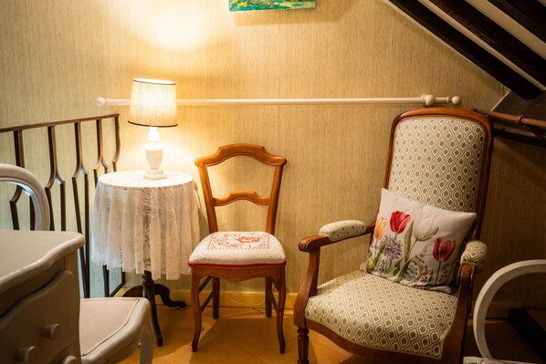 A room with a wooden chair, a table with a lace tablecloth, a lamp, and a railing.