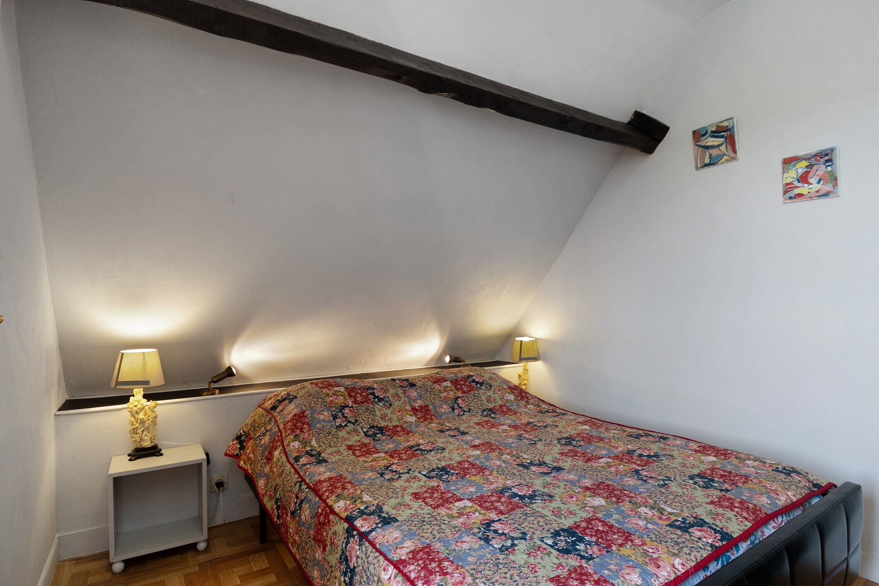 Um quarto com uma cama, duas luminárias de cabeceira, uma mesinha de cabeceira e uma prateleira na parede.