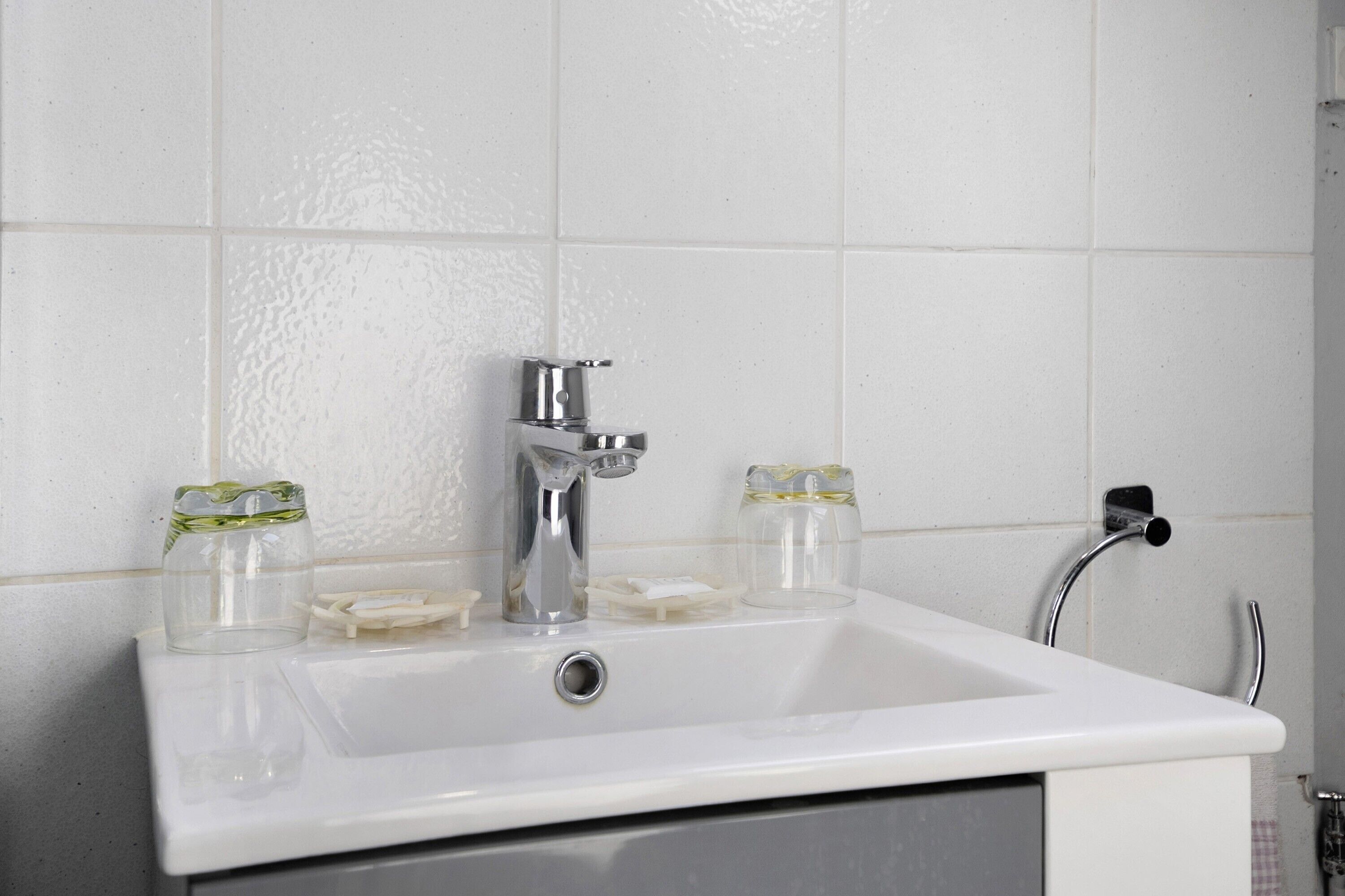 Een badkamermeubel met een chromen kraan, twee glazen zeepdispensers en een handdoekrek.