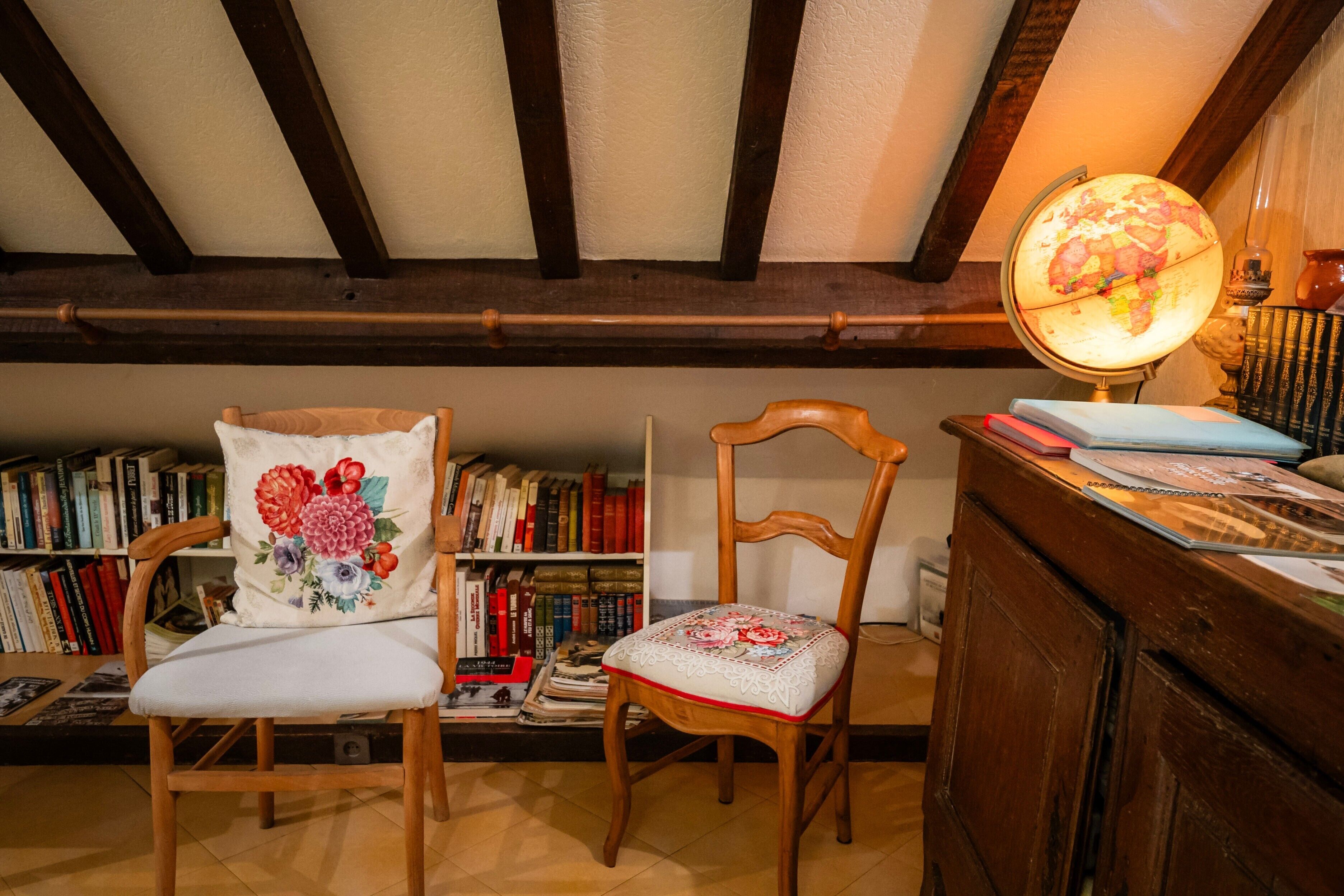 Een gezellige leeshoek met twee houten stoelen, een boekenplank vol boeken, een globe lamp en een houten kast.