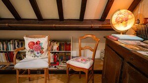 Un rincón acogedor para leer con dos sillones de madera, una estantería llena de libros, una lámpara globo y un mueble de madera.