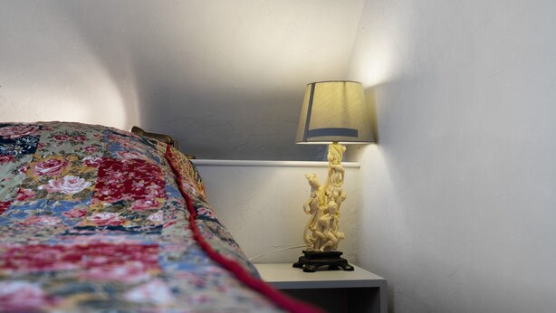 Una cama con una colcha estampada, una mesita de noche con una lámpara y una pared.