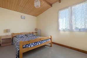 A bedroom with a wooden bed, a desk, and a window with patterned curtains. - Duplex No. 2345 – 40m² – Seaside Residence (Port-des-Barques)