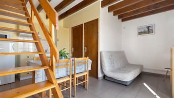 Une pièce avec un escalier en bois, un coin repas avec une table et des chaises, un canapé et un coin cuisine équipé d’appareils électroménagers.