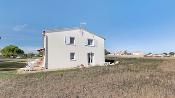 Un bâtiment à deux étages, doté d’un toit plat, d’un petit porche avec des chaises blanches et surplombant un ciel d’un bleu limpide.