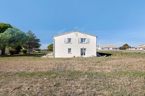 Une maison de plain-pied à l’extérieur blanc, dotée de deux fenêtres avec volets et d’un petit porche.