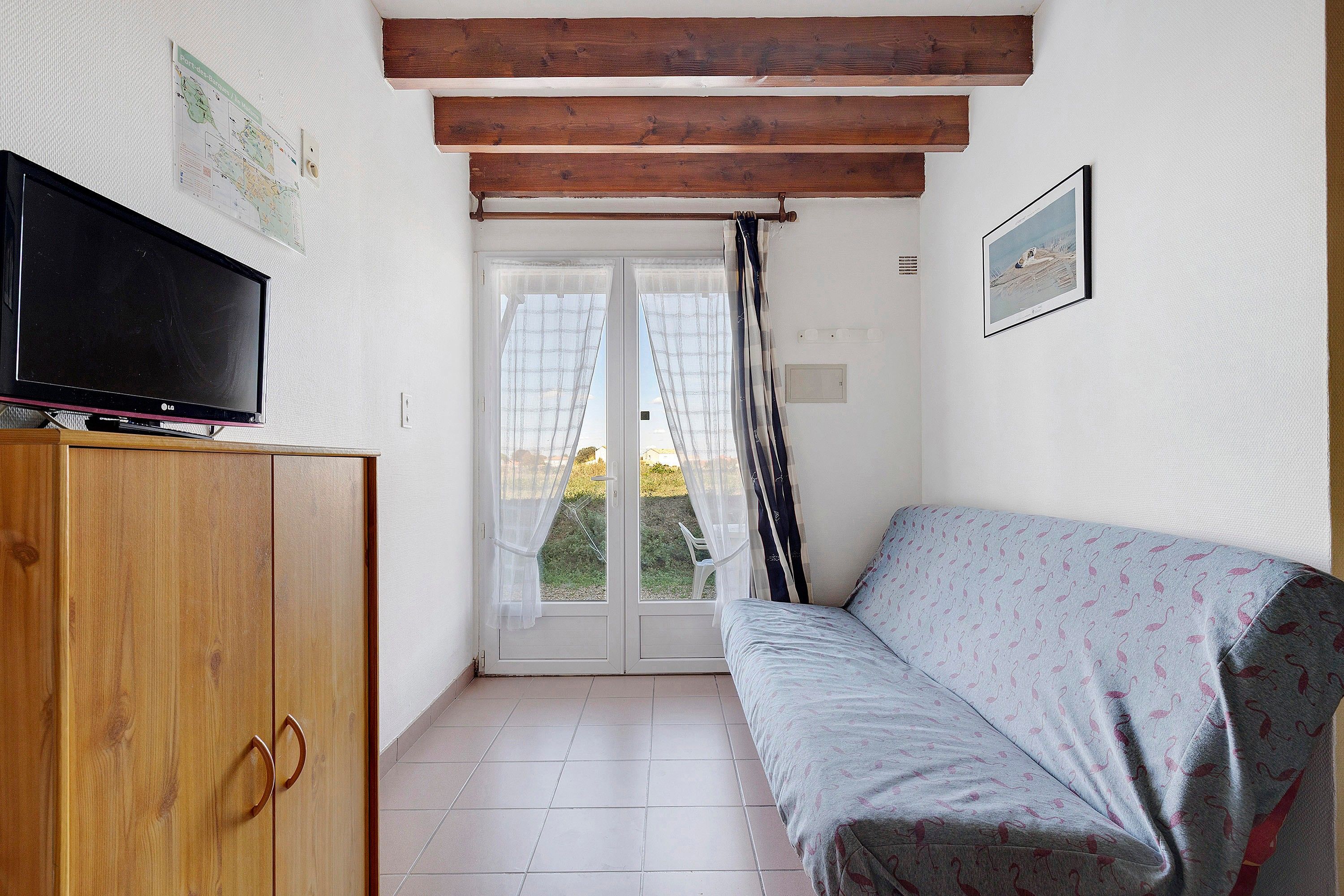 Une petite pièce avec un meuble en bois, une télévision, un canapé et une porte donnant sur l’extérieur.