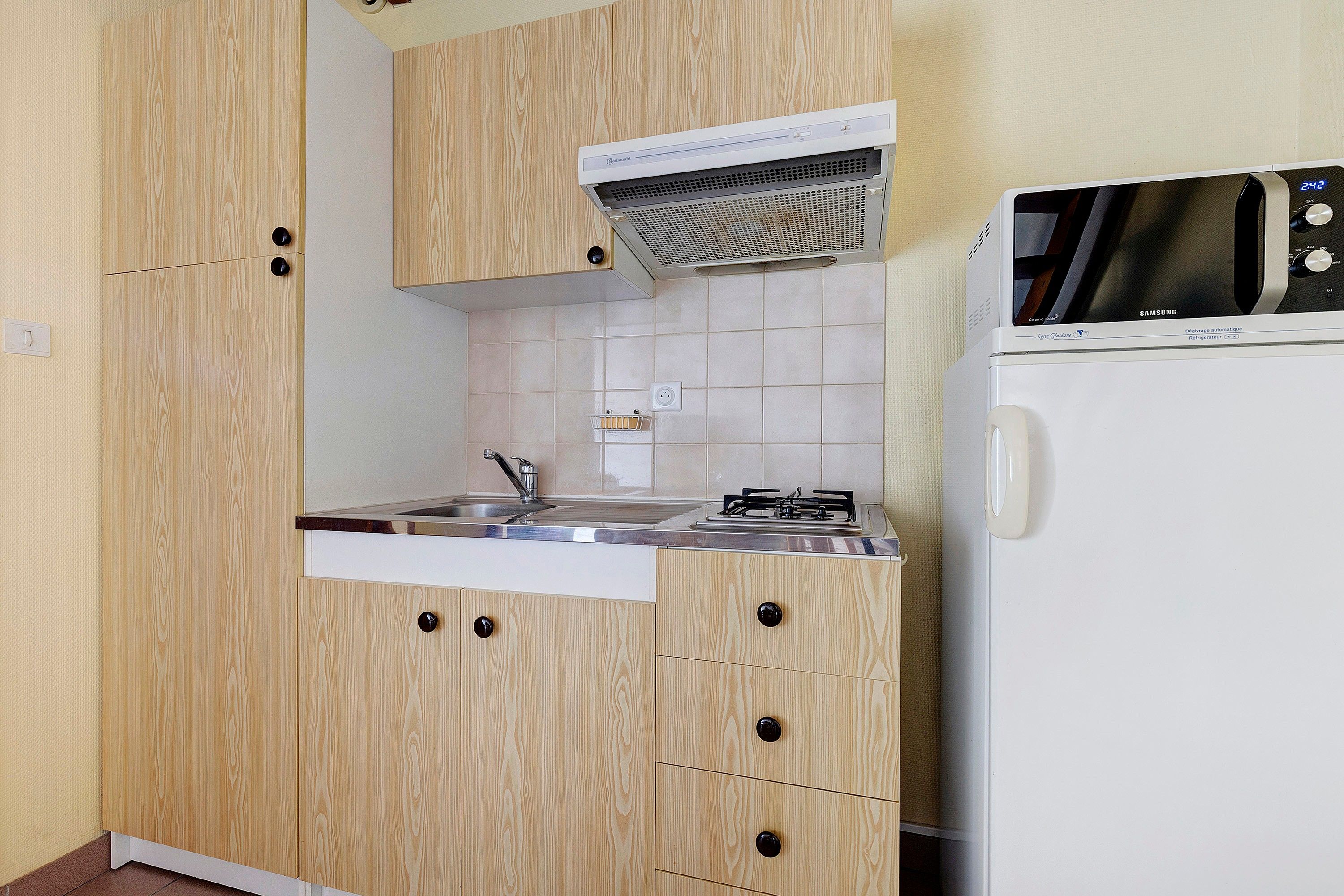 Eine kleine Küche mit Holzausstattung, einem eingebauten Herd und einem weißen Kühlschrank.