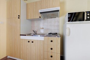 A compact kitchen with wooden cabinets, a built-in stove, and a white refrigerator. - Duplex No. 2345 – 40m² – Seaside Residence (Port-des-Barques)