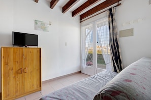 A bedroom with a bed, a wooden wardrobe, a television on top, a sliding glass door, and a map on the wall. - Duplex No. 2345 – 40m² – Seaside Residence (Port-des-Barques)