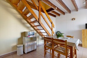 A dining area with a wooden staircase, a table set for two, and a small cabinet with a television. - Duplex No. 2345 – 40m² – Seaside Residence (Port-des-Barques)