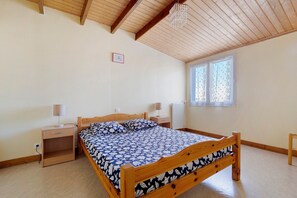 A bedroom with a wooden bed, bedside tables, a window with curtains, and a wooden ceiling. - Duplex No. 2345 – 40m² – Seaside Residence (Port-des-Barques)