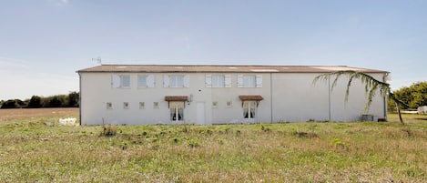 Un edificio de una sola planta con techo plano, varias ventanas con contraventanas y un pequeño porche.