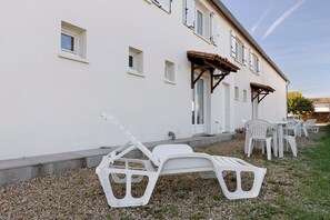 A white building with multiple windows and a covered outdoor seating area with white plastic chairs. - Duplex No. 2345 – 40m² – Seaside Residence (Port-des-Barques)