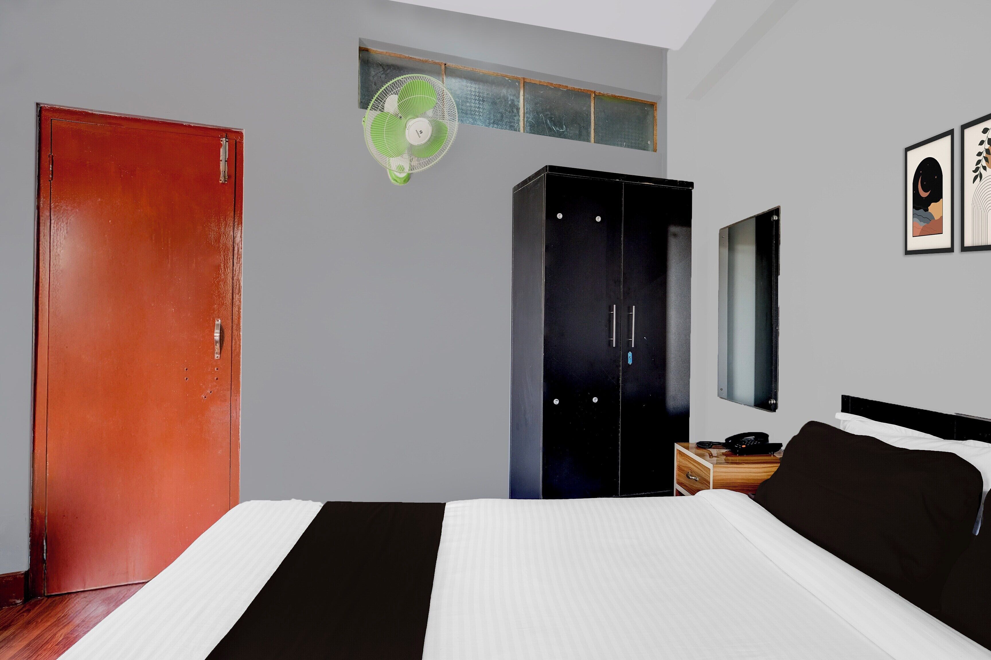 Une chambre à coucher avec un lit, une armoire, un miroir et une petite table sur laquelle se trouve un téléphone.