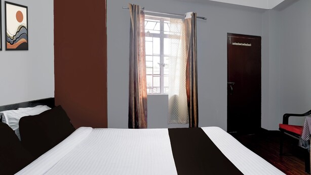 A hotel room with a bed, a chair, a wardrobe, and a window with curtains.