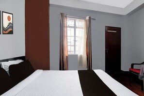 A hotel room with a bed, a chair, a wardrobe, and a window with curtains.