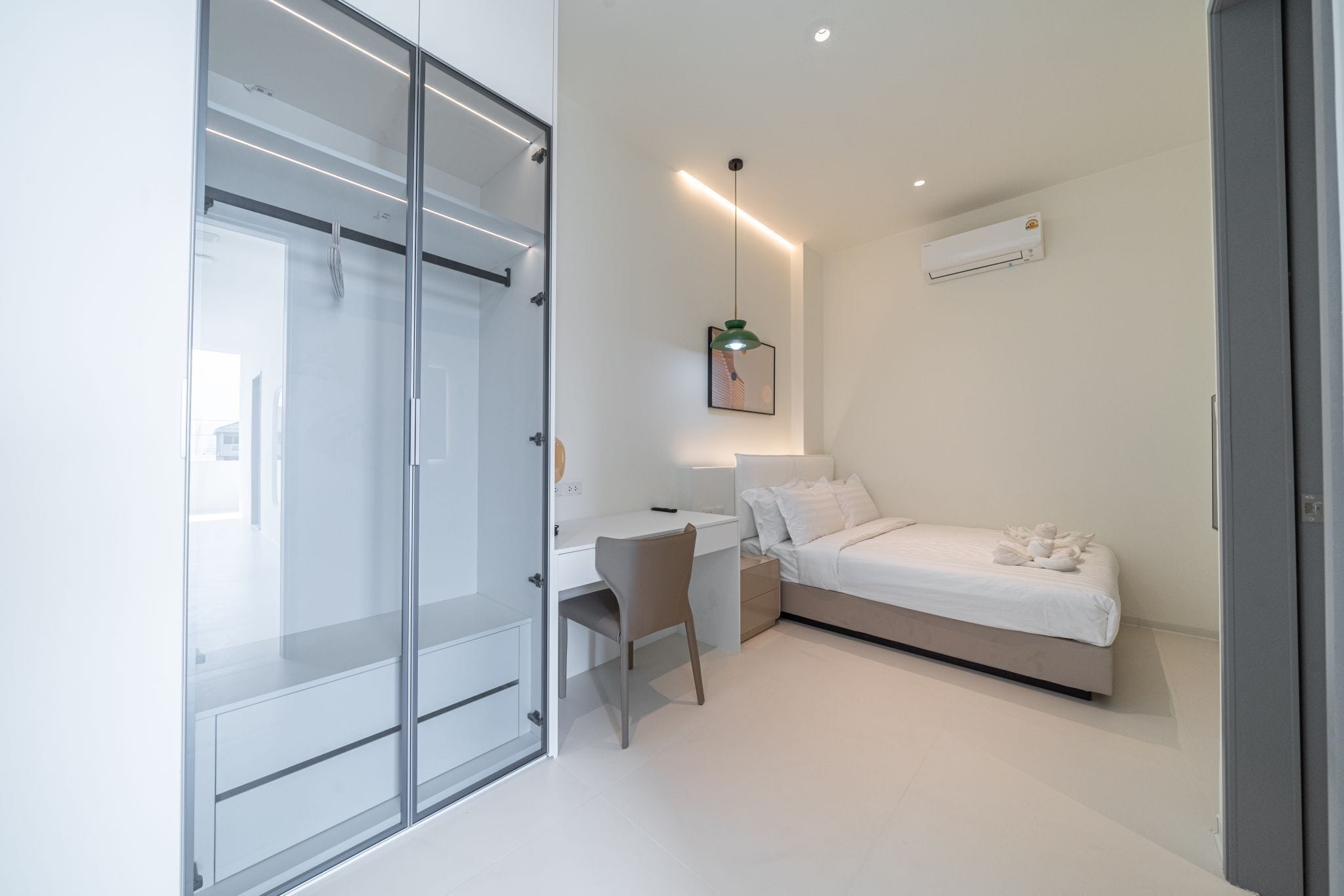 Quarto moderno com divisória de vidro, escrivaninha, cama e luminária pendente.