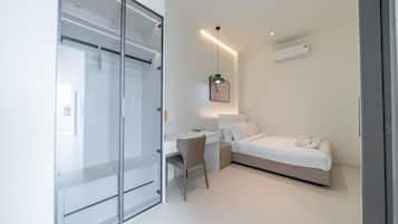 Quarto moderno com divisória de vidro, escrivaninha, cama e luminária pendente.