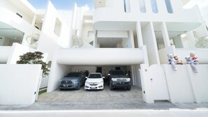 Un edificio moderno con fachada blanca, un acceso cubierto y tres automóviles estacionados.