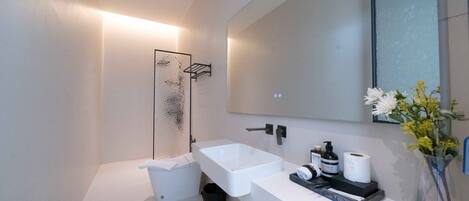 A modern bathroom with a white sink, a large mirror, and a shower enclosure.