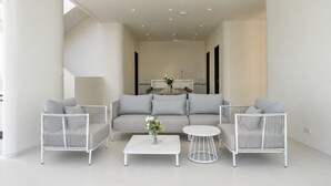 A modern living room with a sofa, two armchairs, a coffee table, and a dining area in the background.