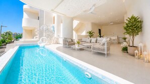 A modern indoor pool area with a clear blue pool, white furniture, and a ceiling fan.