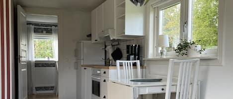 Une cuisine moderne avec des meubles blancs, une table à manger avec des chaises et une vue sur la verdure à l’extérieur.