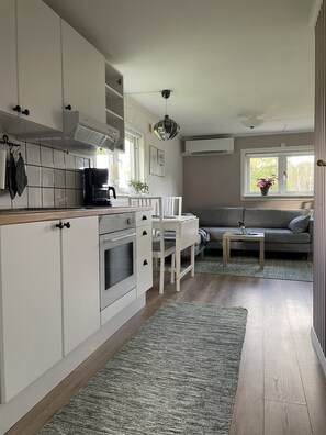 A modern kitchen with white cabinets, a coffee machine, and a dining area with a grey sofa and a small table.