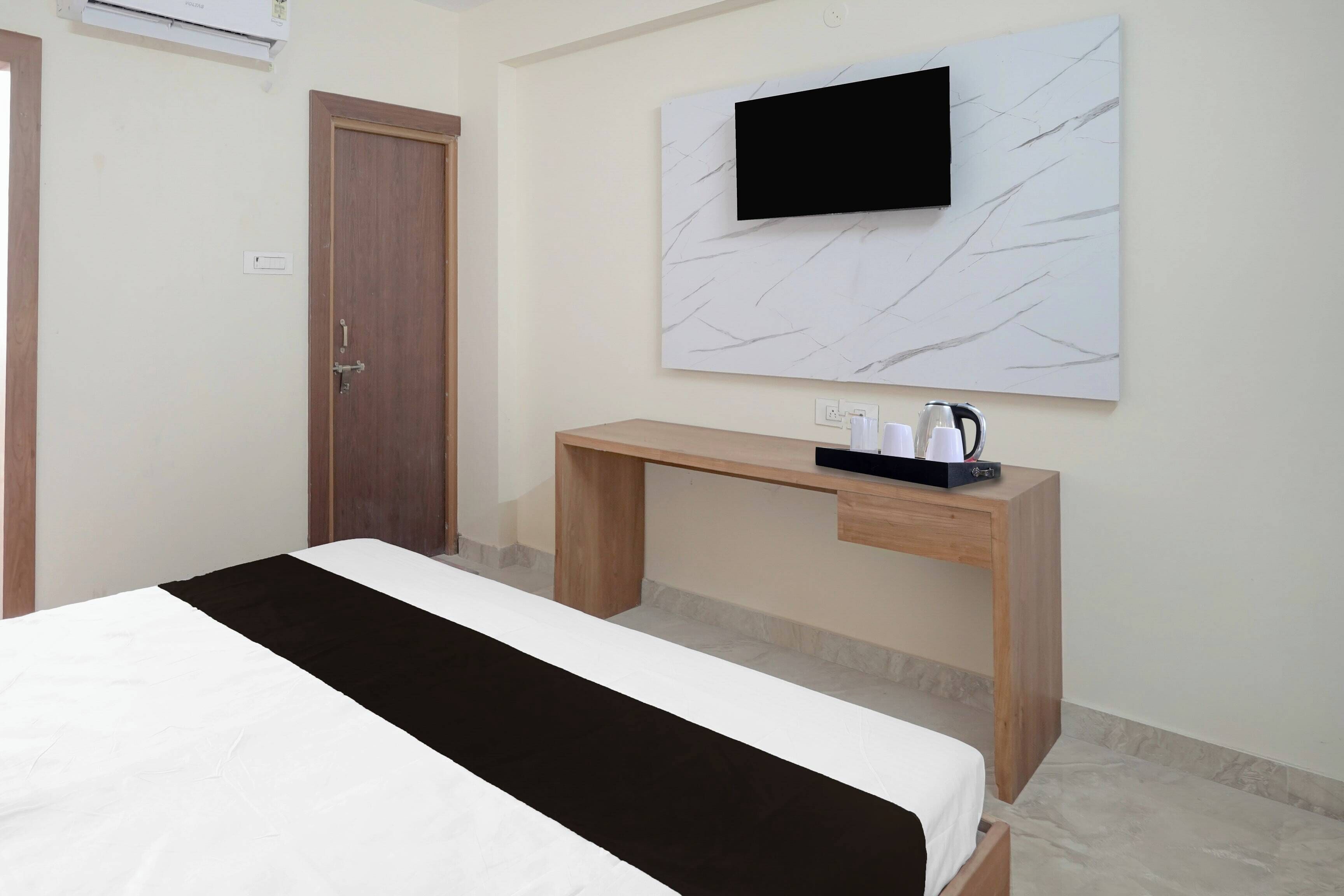 Habitación de hotel con cama, escritorio de madera, televisor montado en la pared y una mesita con hervidor y tazas.