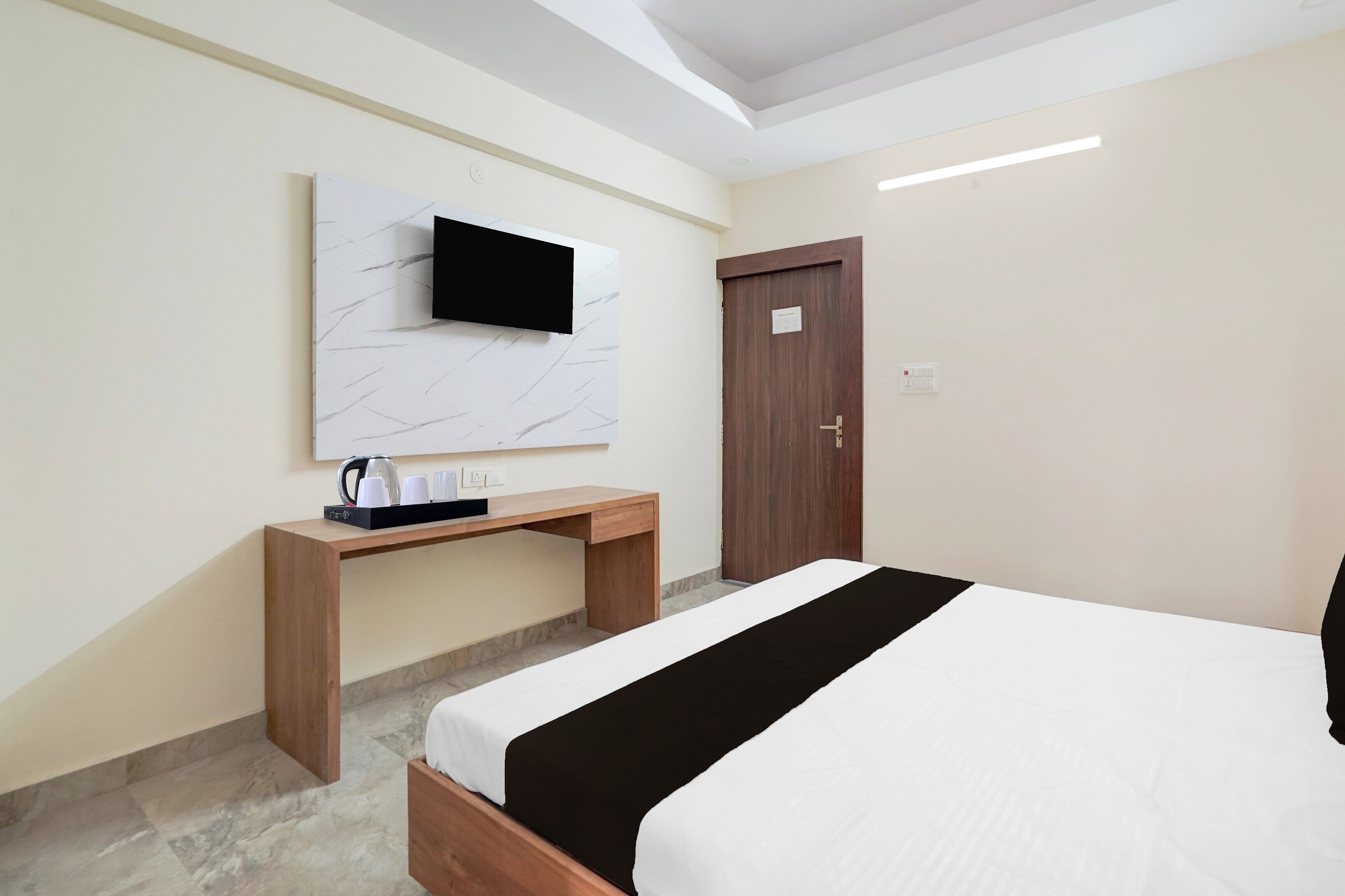 Une chambre d’hôtel avec un lit, un bureau en bois, un téléviseur à écran plat fixé sur un mur en marbre et une porte avec une pancarte.