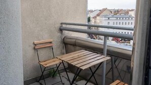 Ein Balkon mit zwei Holztischen und -stühlen, einem Metallgeländer und Blick auf Gebäude in der Ferne.