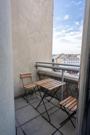 A balcony with two wooden tables and chairs, a metal railing, and a view of buildings in the distance. - Mavie Hotel Domenig (Vienna)