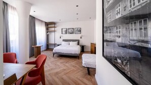 Ein modernes Hotelzimmer mit einem großen Bett, einem Essbereich mit roten Stühlen und einem großen Fenster mit Blick auf ein Gebäude.