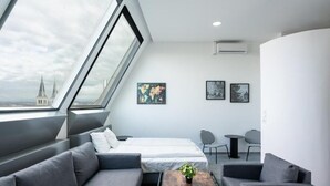Ein modernes Hotelzimmer mit großem Fenster, einem Bett, einer Couch, einem kleinen Tisch und zwei Stühlen.