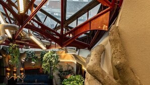 Ein Innenraum mit hohen Decken, einer zentralen Treppe, einem Essbereich und hängenden Pflanzen.