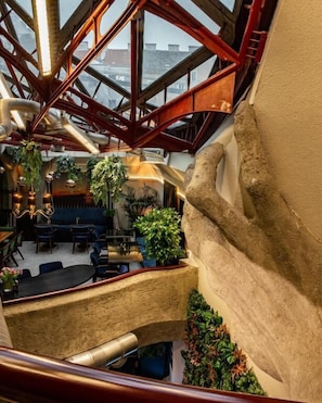 A high-ceilinged interior with a central staircase, dining area, and hanging plants. - Mavie Hotel Domenig (Vienna)
