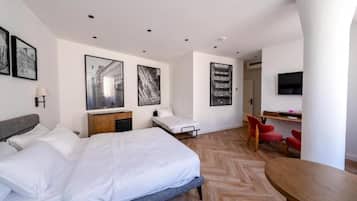 Ein modernes Hotelzimmer mit einem großen Bett, einem Schreibtisch und einem Fernseher. An den Wänden befinden sich gerahmte Bilder und der Boden hat ein Fischgrätenmuster.