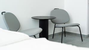 Una habitación con una mesa redonda, dos sillas, una cama y una pared blanca.