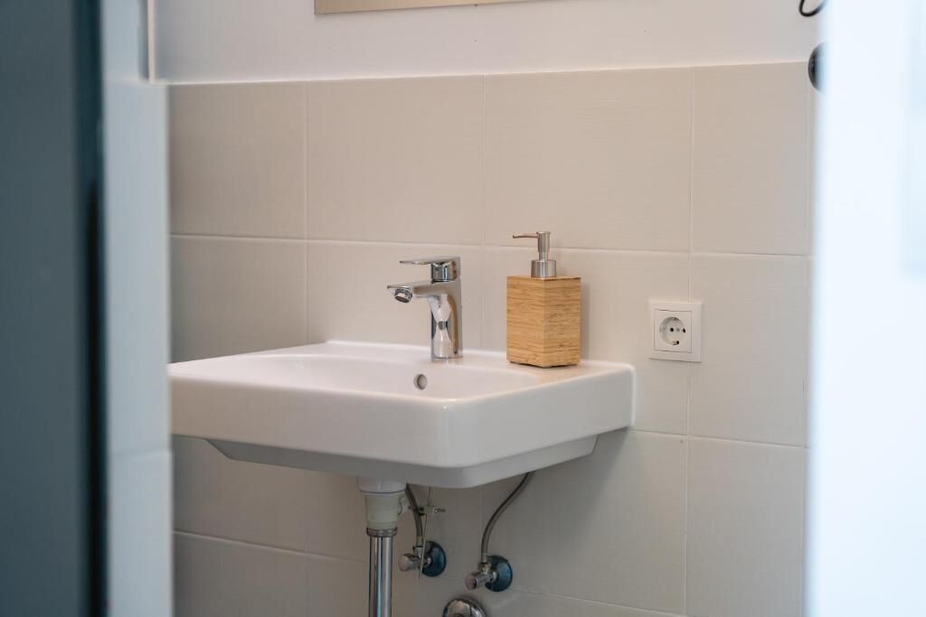 Ein Badezimmer mit einem weißen Waschbecken, einem Holzdosierer für Seife und einer sichtbaren Steckdose.