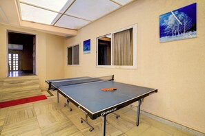A ping pong table with wheels, a red carpet, and a painting of a snowy landscape on the wall. - Collection O Gold Valley (Lonavala)