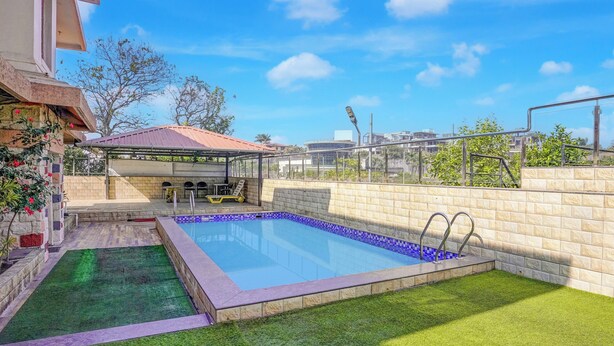 A swimming pool with a small deck area, a covered seating area, and a view of the surrounding buildings. - Collection O Gold Valley (Lonavala)